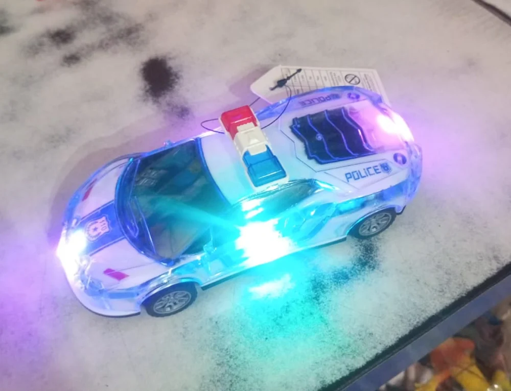 A light-up toy police car glowing blue and purple on a worn tabletop.